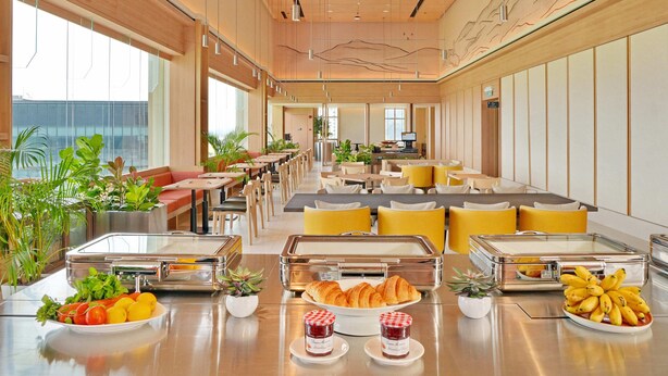 Un comedor amplio de hotel con varias mesas, sillas y un bufé con comida y bebidas.