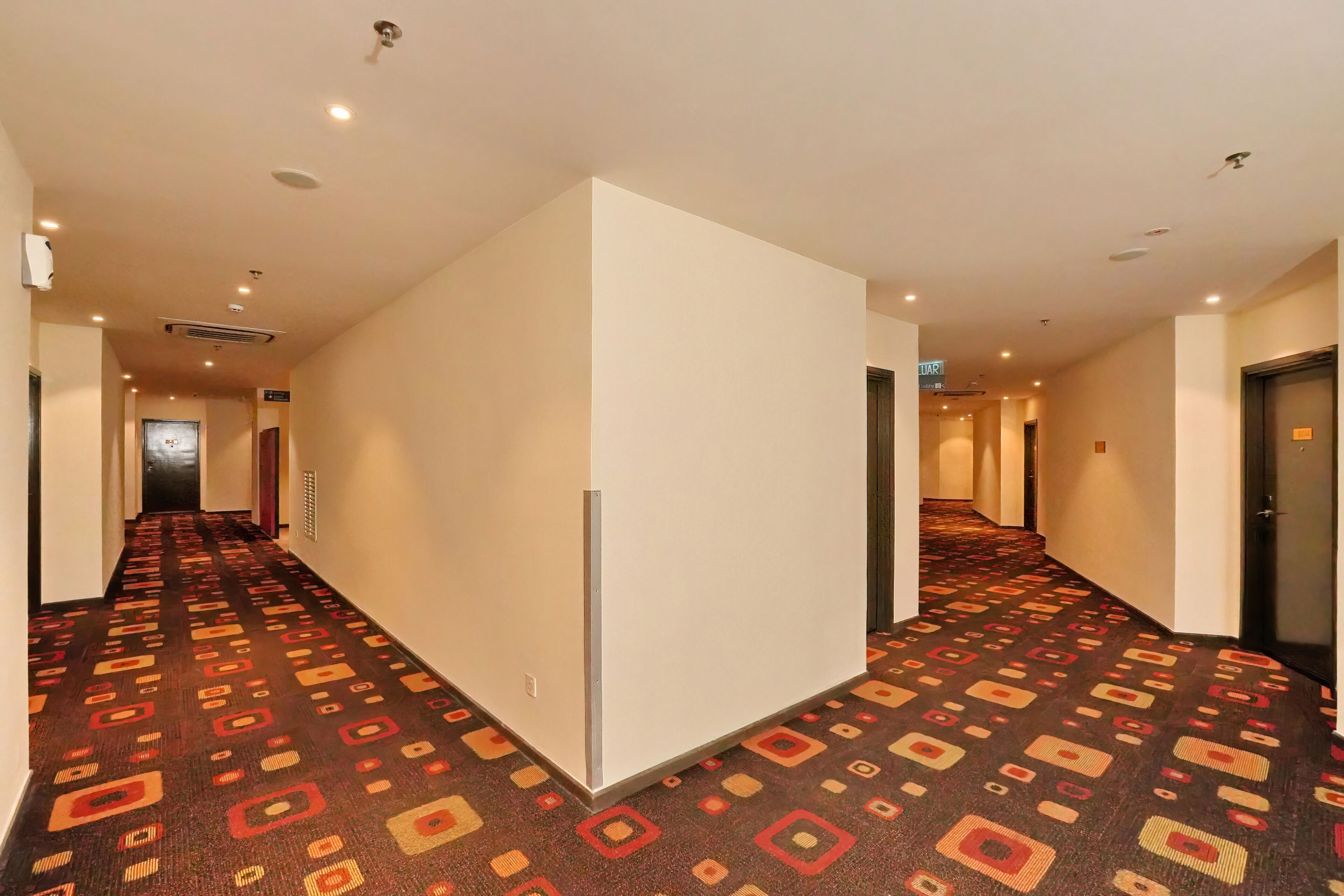 A hotel corridor with patterned carpet, white walls, and doors leading to rooms.
