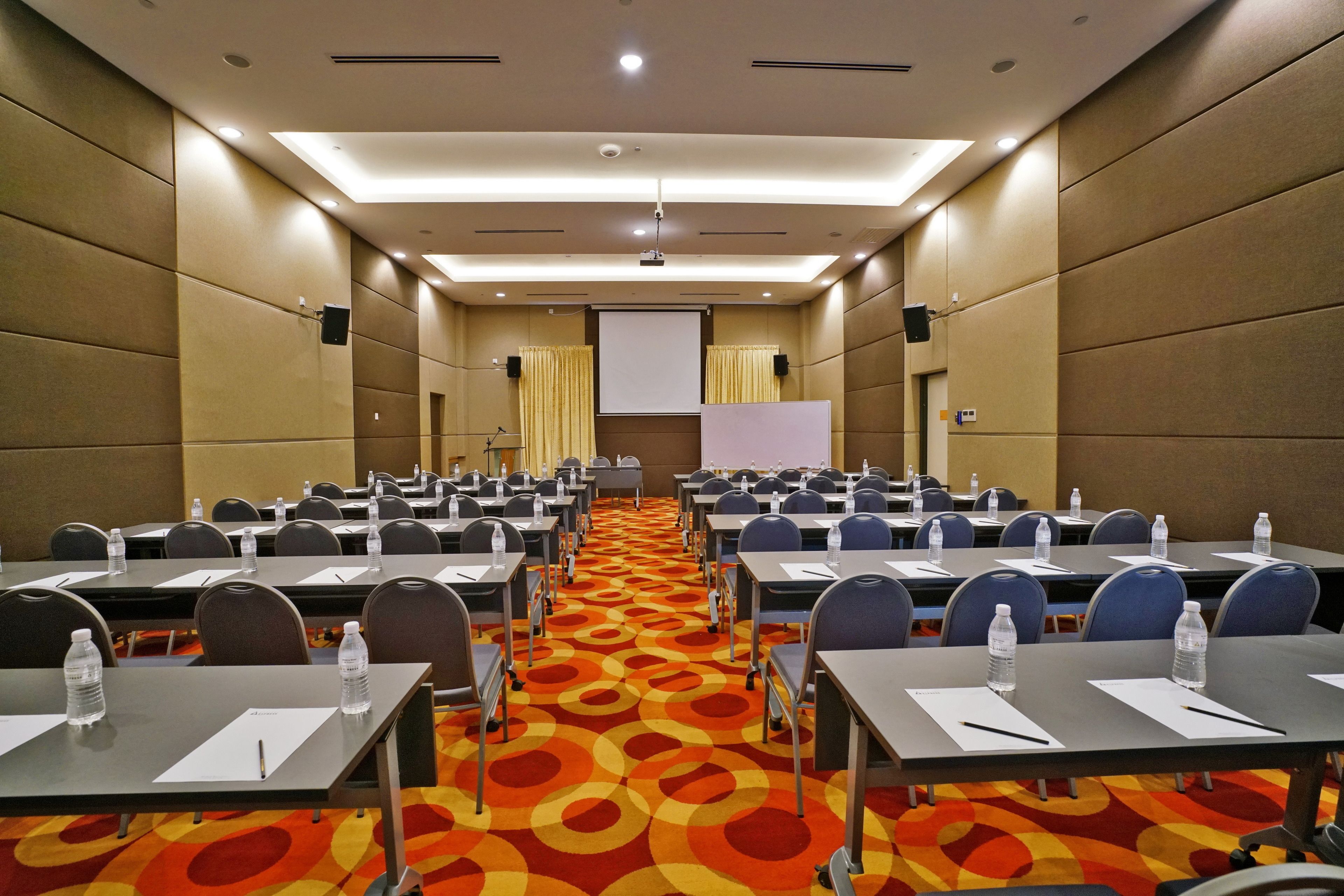 A conference room with rows of tables, chairs, and a projector screen at the front.