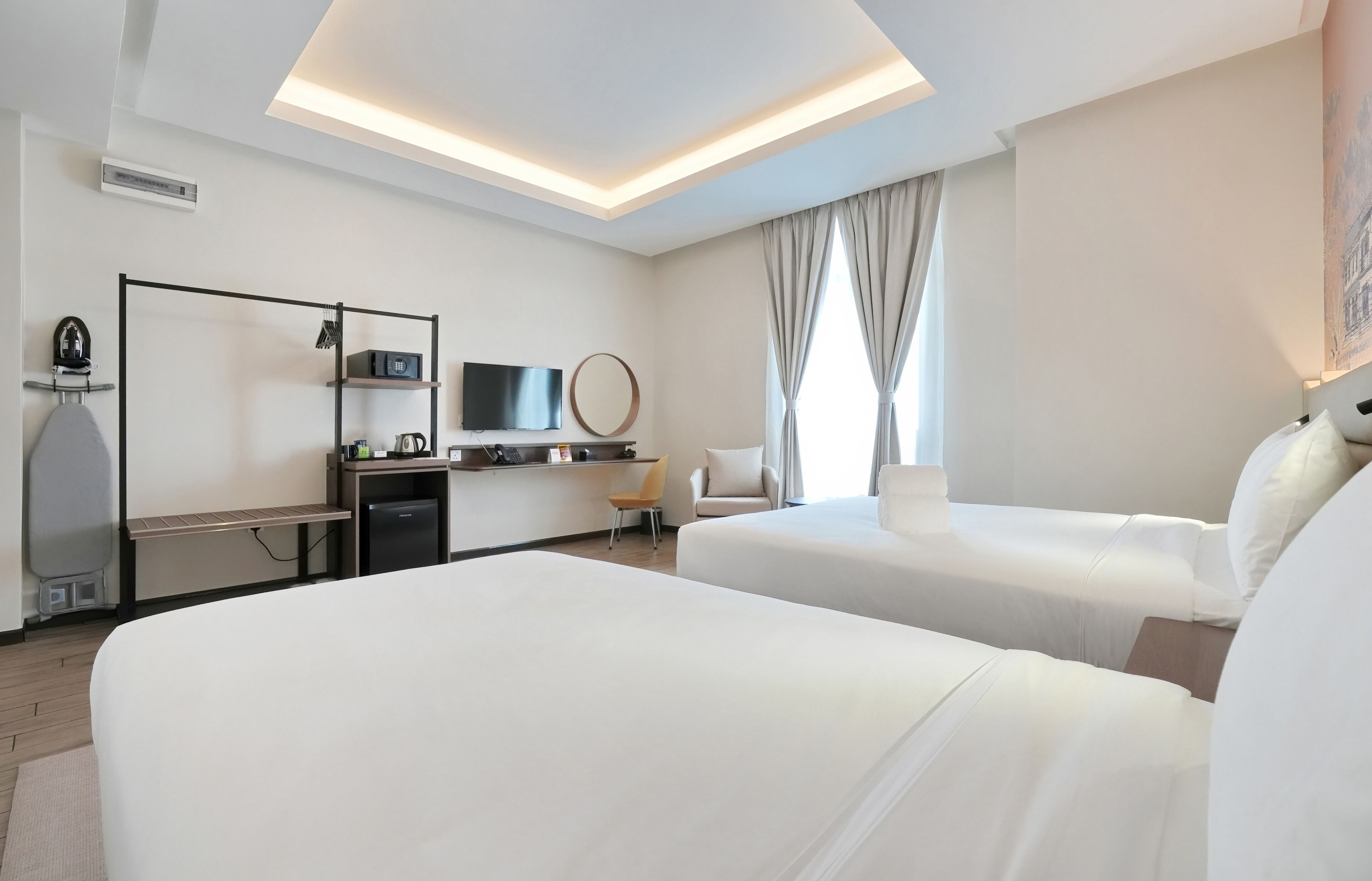 Habitación de hotel con dos camas, un escritorio, televisión de pantalla plana, cafetera y una pequeña zona de estar con una silla y lámpara.
