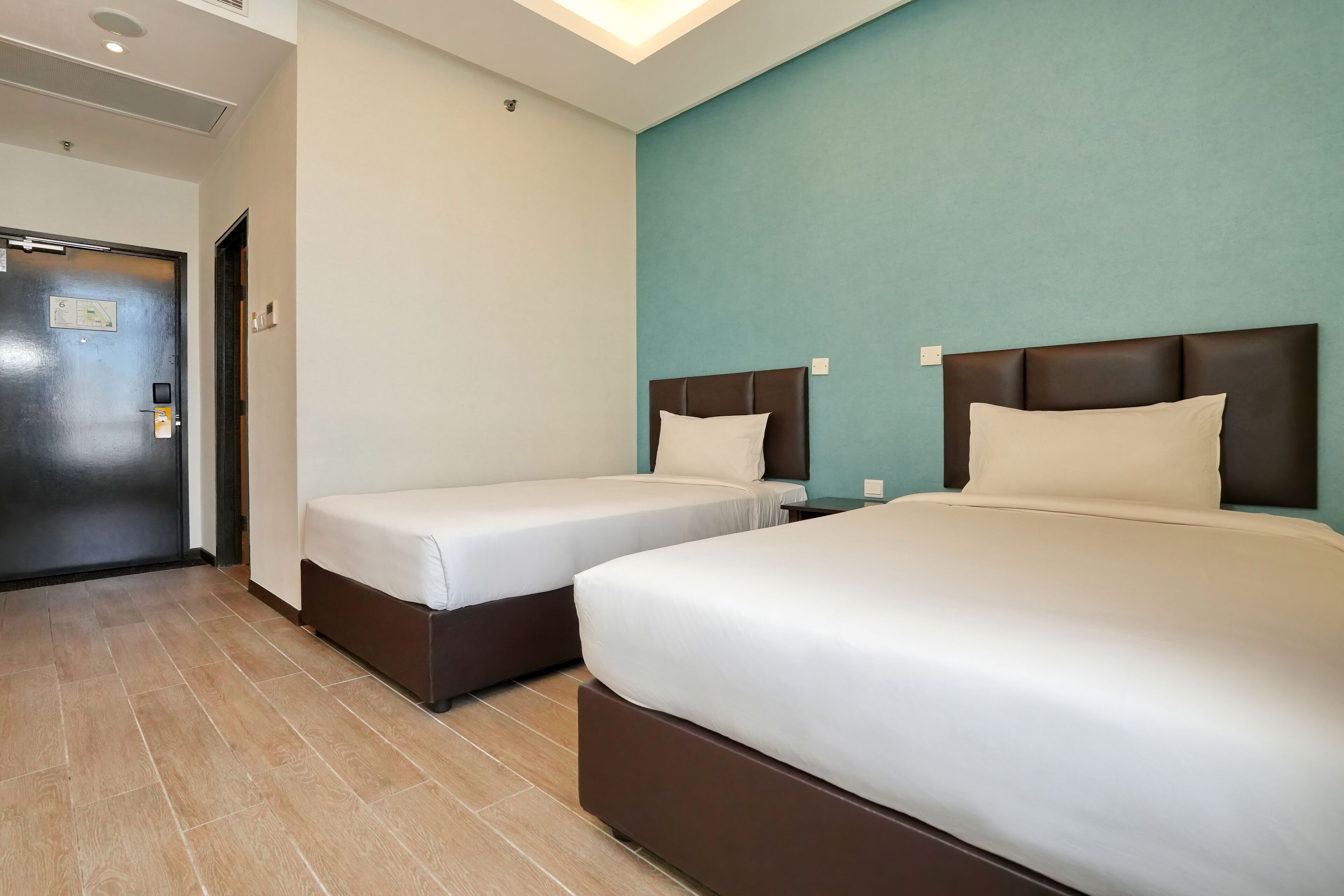 A hotel room with two beds, a door, and a light blue accent wall.