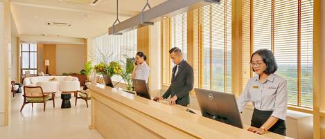 A reception area with a wooden reception desk, two employees at workstations, and a seating area with chairs and a table.