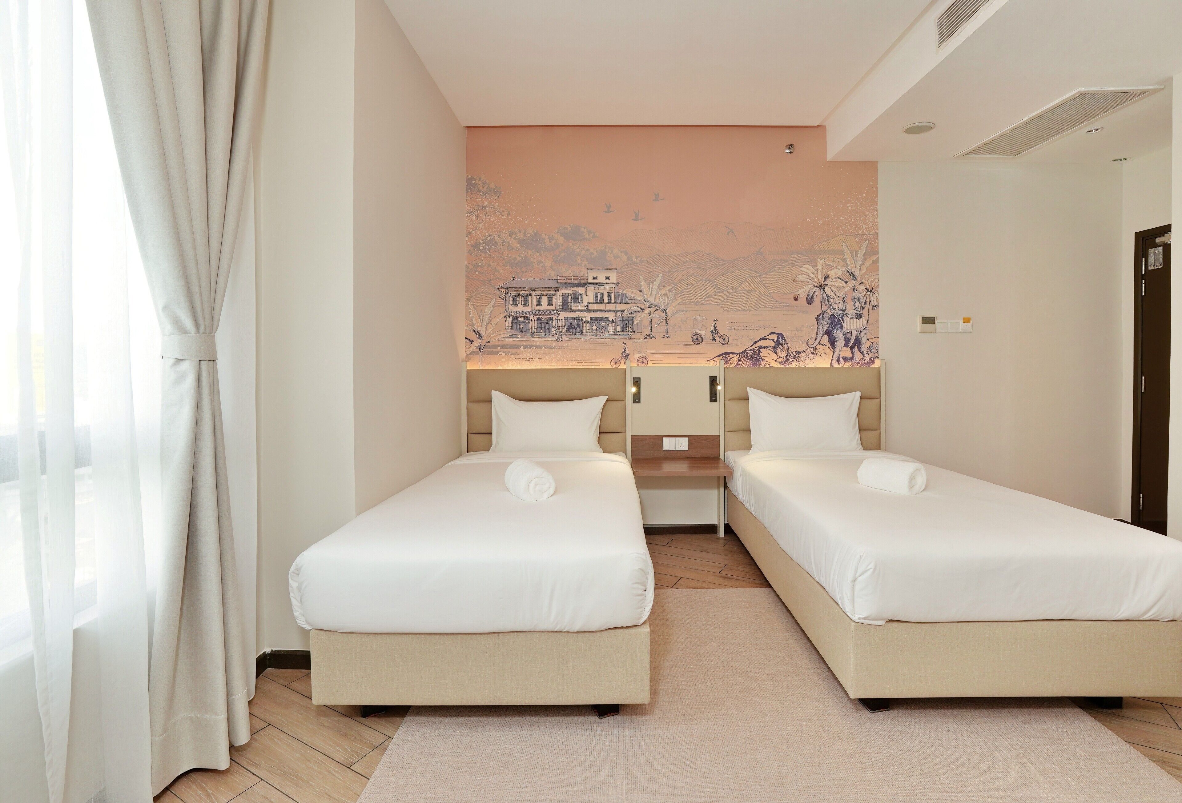 A hotel room with two single beds, a small desk, and a mural on the wall.
