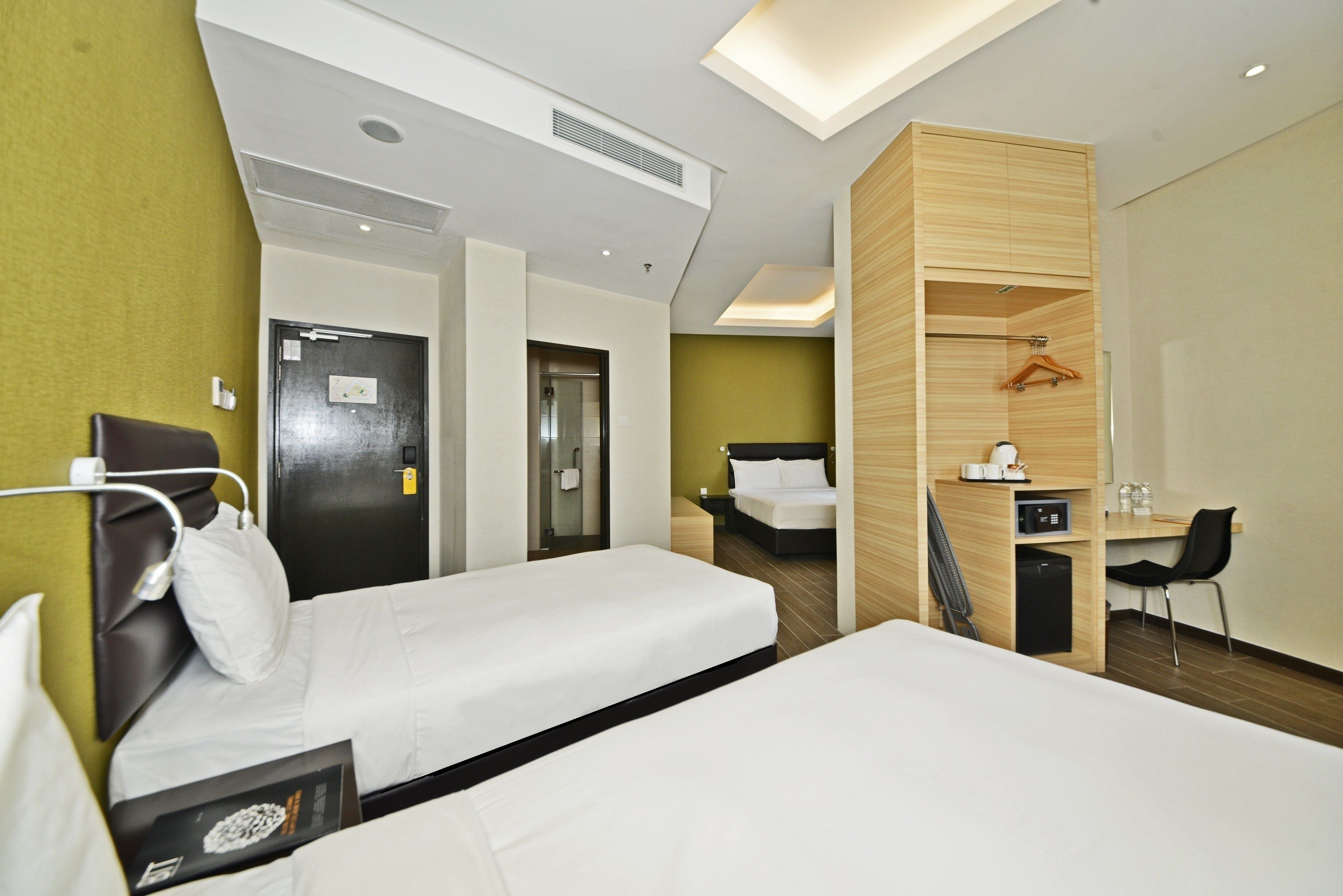 A hotel room with two beds, a desk, a chair, a wardrobe, and a bathroom.