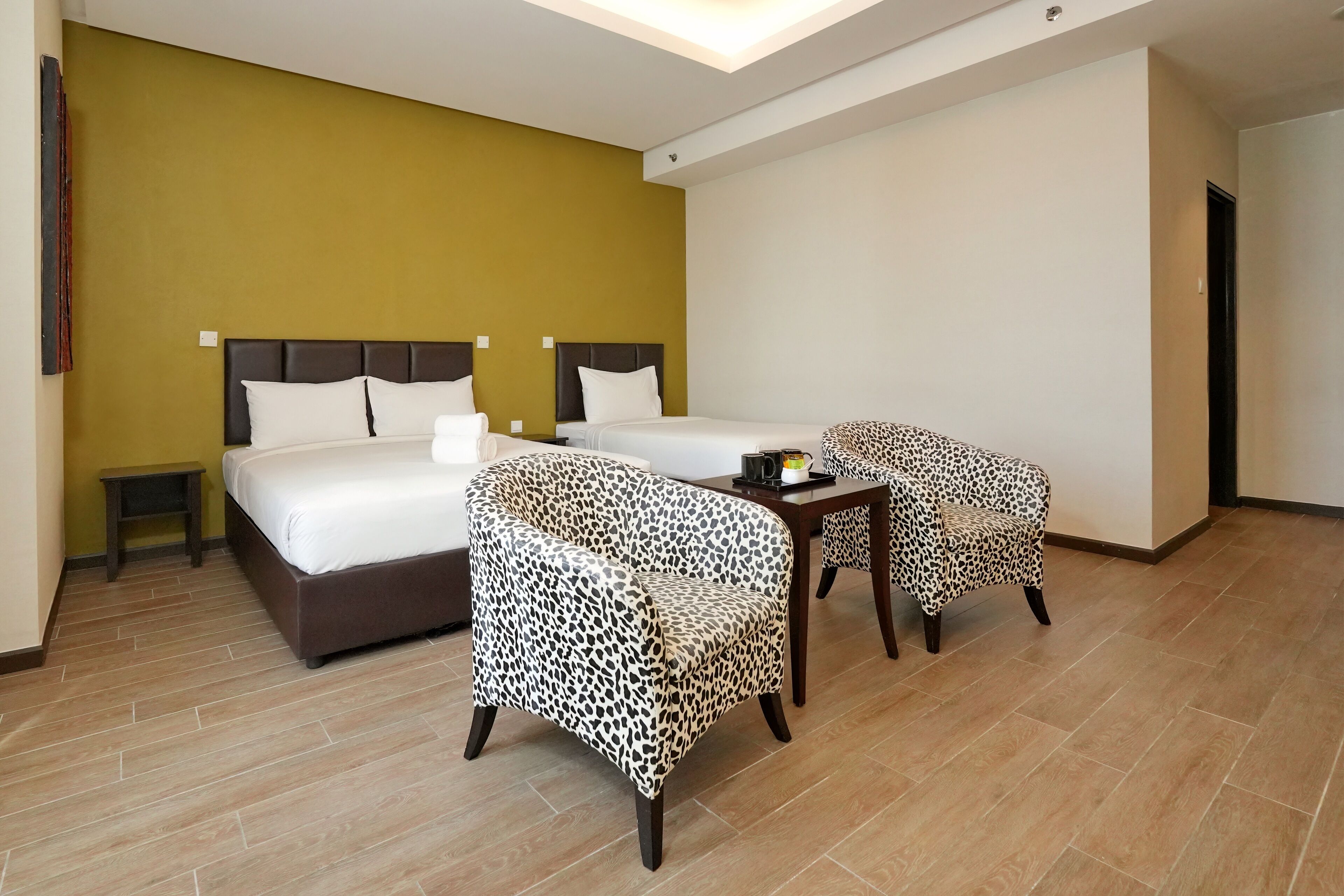 A hotel room with two beds, a small table, leopard print chairs, and a nightstand.
