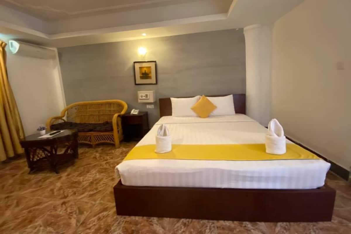 A hotel room with a large bed, a chair, a small table, and a picture on the wall.