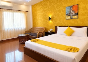 Habitación de hotel con cama, una silla, una mesita y un cuadro en la pared.