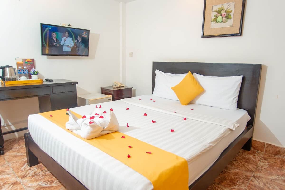 A hotel room with a bed, a desk, a television, and a framed picture on the wall.