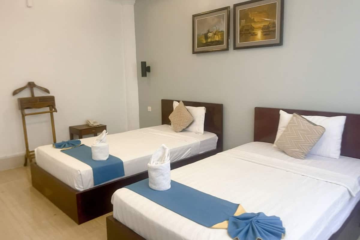 A hotel room with two beds, a wooden hanger, a bedside table with a phone, and two framed pictures on the wall.
