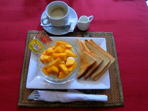 A breakfast setting with toast, a bowl of fruit, a cup of coffee, and condiments on a placemat. - Best Central Point Hotel (Phnom Penh)