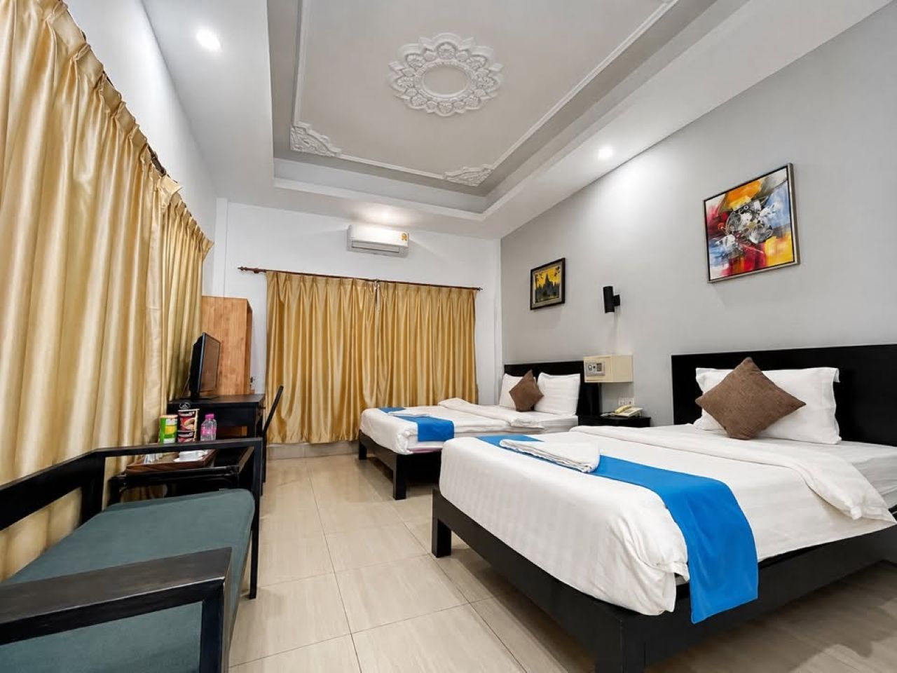 A hotel room with two beds, a desk, a chair, a wardrobe, and a painting on the wall.