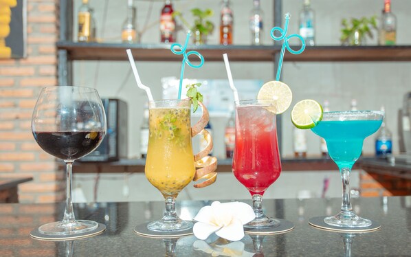 Four different cocktails on a bar counter with a brick wall and shelves in the background.