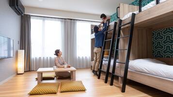 Habitación de hotel con literas, un escritorio con dos sillas, una lámpara de pie y un ventanal con cortinas.