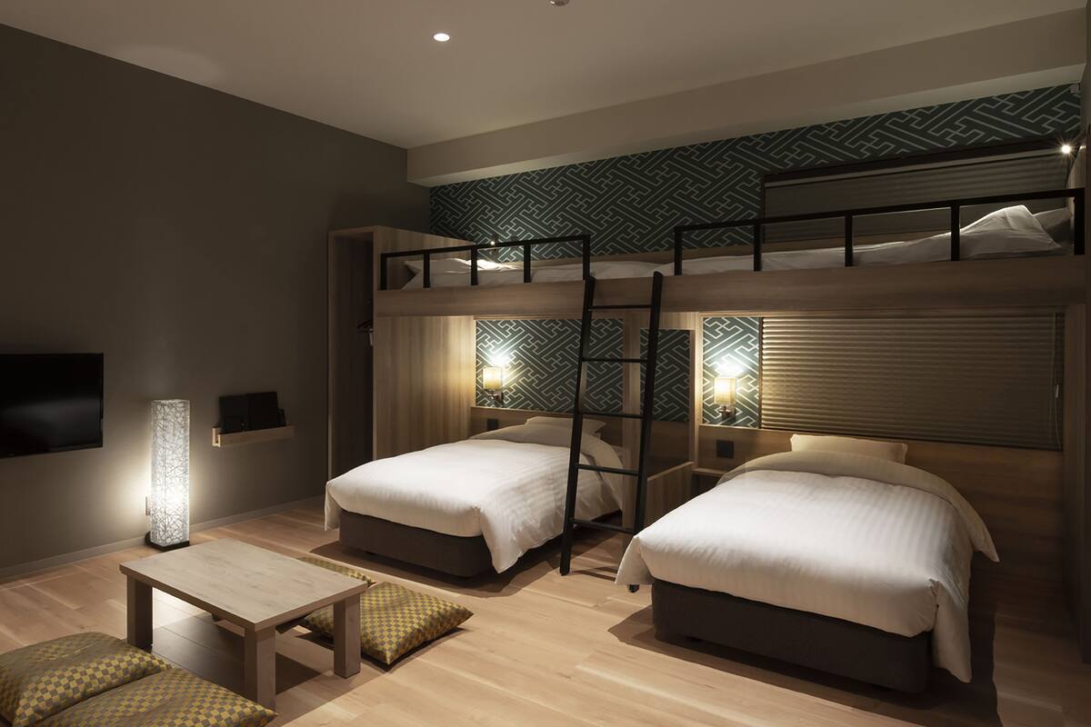 A modern hotel room with bunk beds, a flat-screen TV, a bedside table, and a lamp.