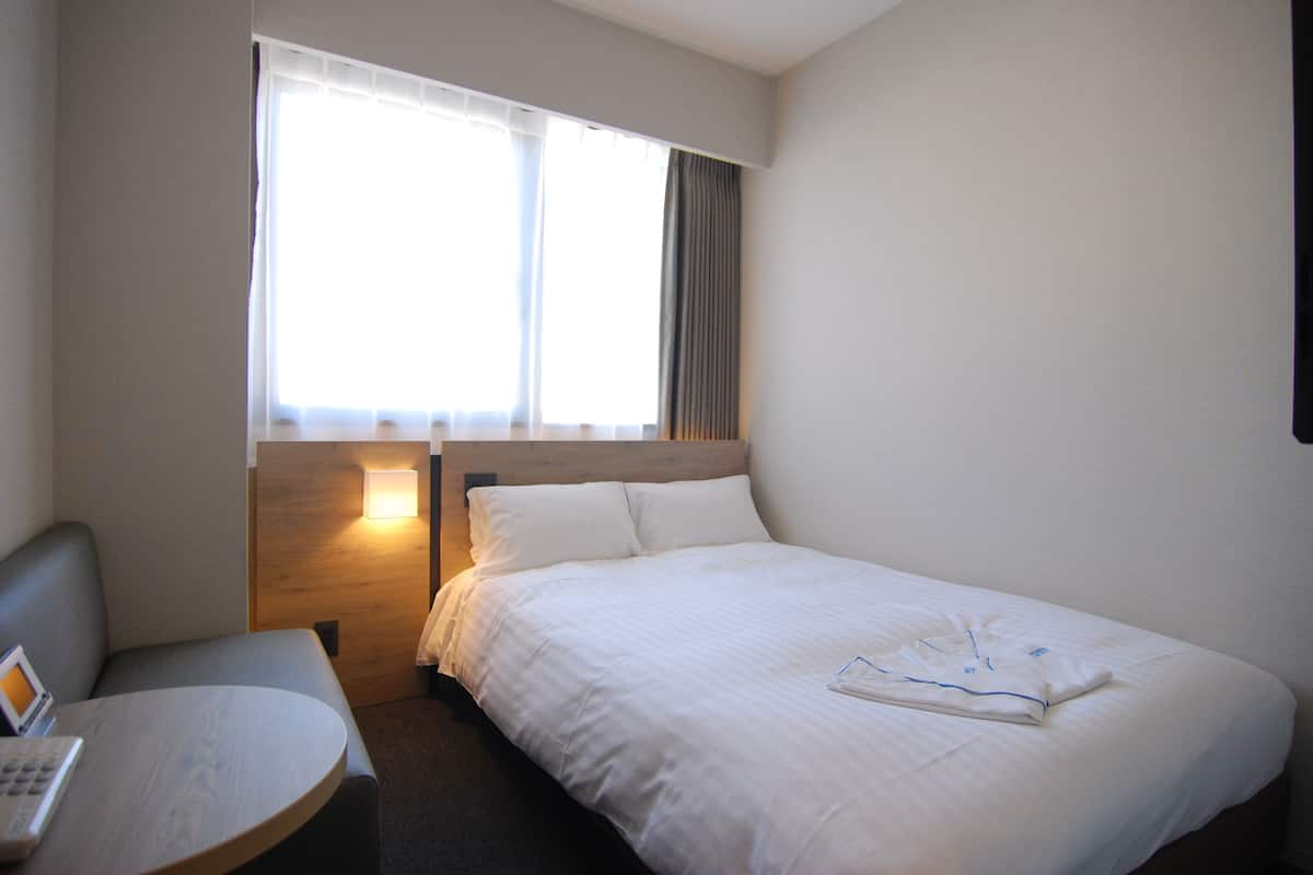 A hotel room with a bed, a desk, and a window with curtains.