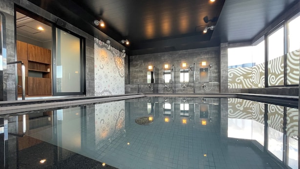 Uma piscina interna moderna com piso de vidro, rodeada por paredes de pedra e armários de madeira.