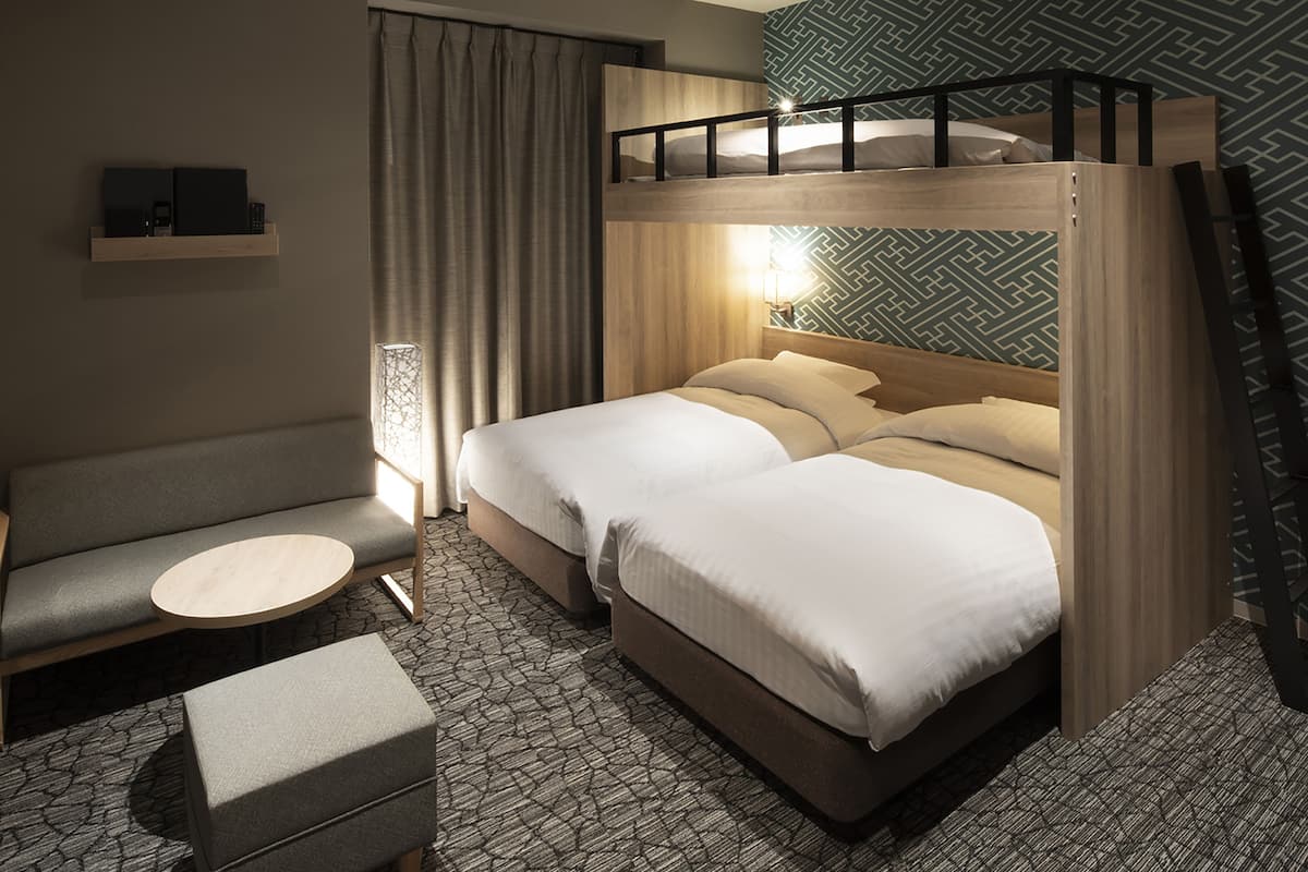 A hotel room with a bunk bed, a sofa, a small round table, and patterned carpet.