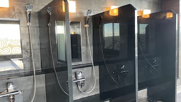 Et moderne badeværelse med tre brusekabiner med glasvægge, hver med en håndbruser og et spejl.