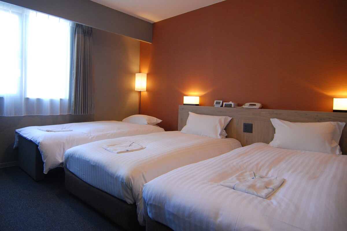 A hotel room with two beds, a round table, and a window with curtains.
