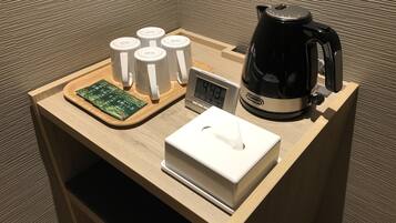 Una mesita de noche de madera con un reloj, un dispensador de pañuelos, una bandeja con tazas y una cafetera.