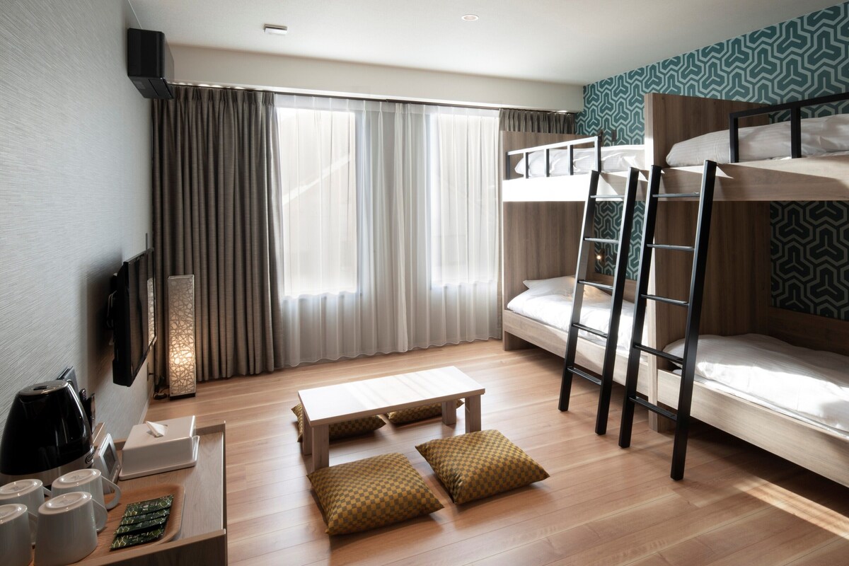 A bunk bed room with a TV, a desk with a kettle, and a patterned wall.