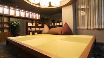 Una habitación con esteras de tatami, cabecera de madera, estantería y planta en maceta.