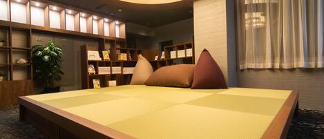 A tatami mat room with a wooden headboard, a bookshelf, and a potted plant.