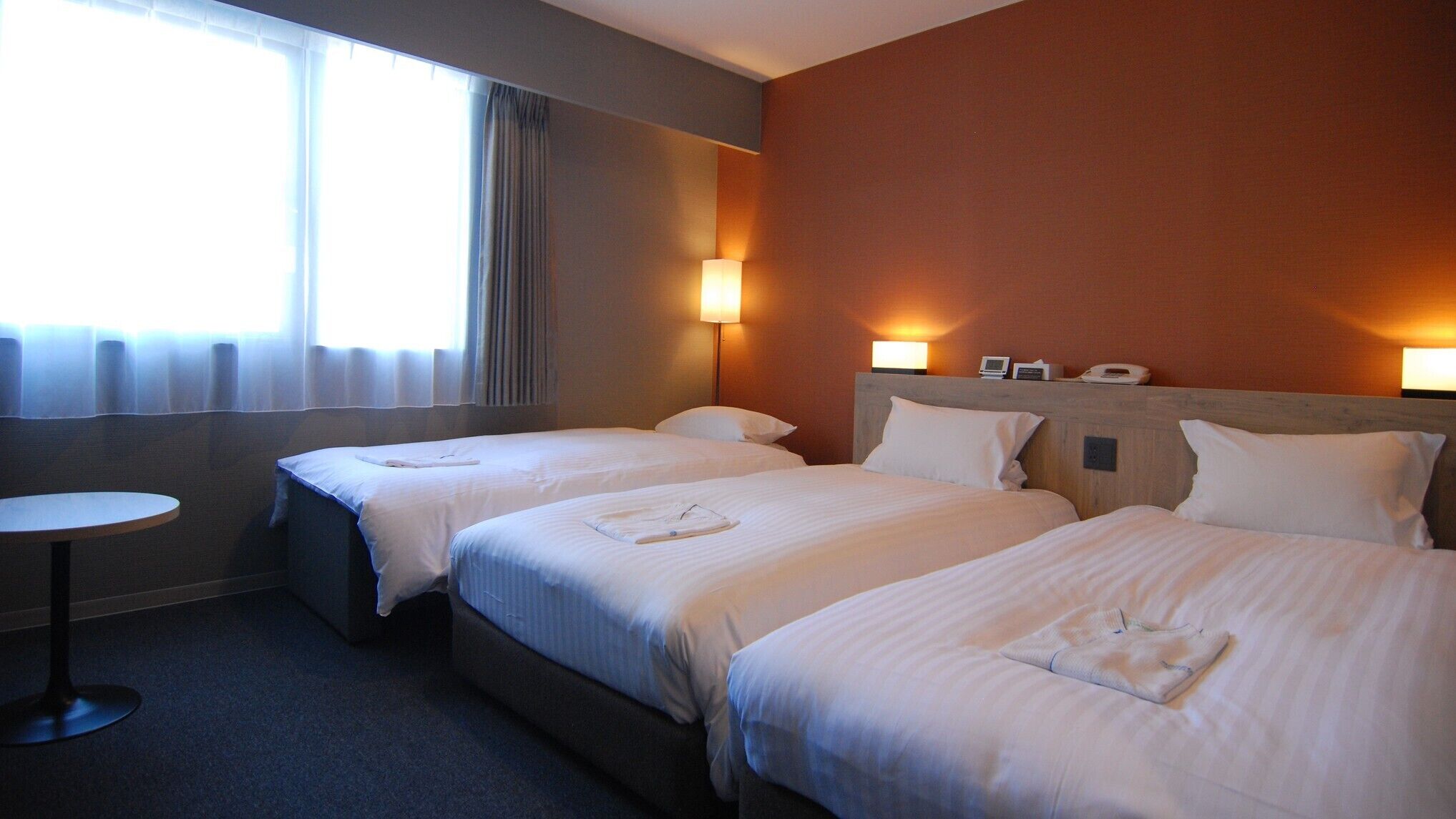 A hotel room with two beds, a round table, and two bedside lamps.