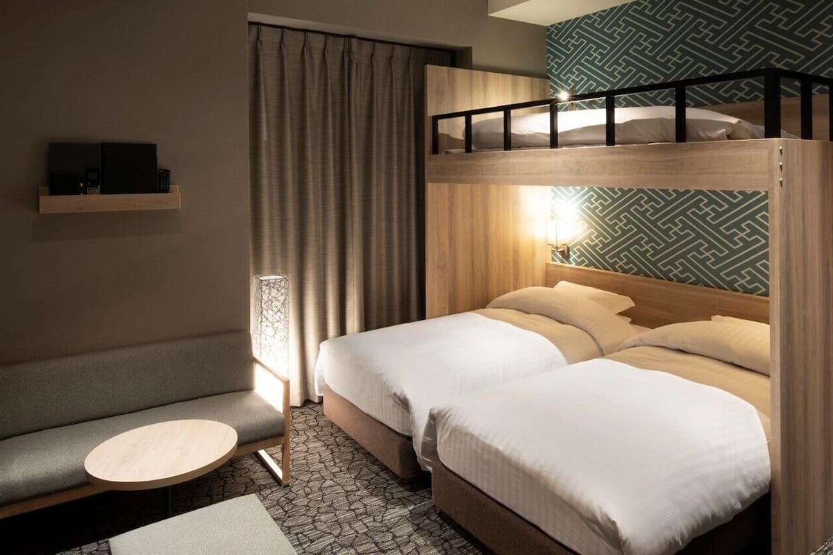 A room with a bunk bed, a sofa, a small round table, and a lamp.