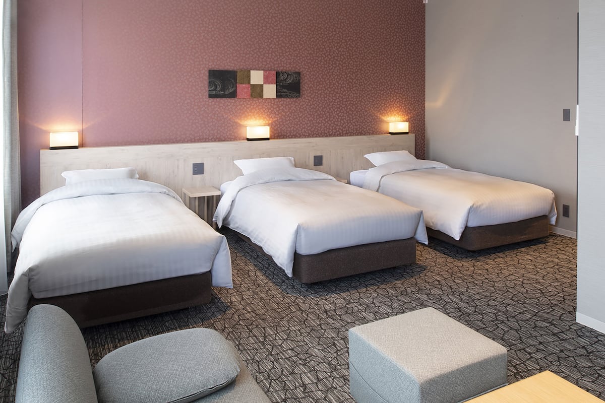 A hotel room with three beds, a sofa, and a small table.