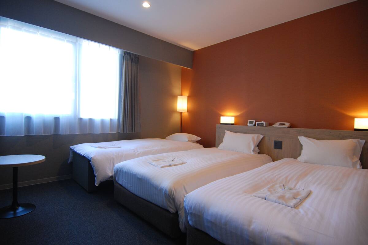 A hotel room with two beds, a round table, and a window with curtains.