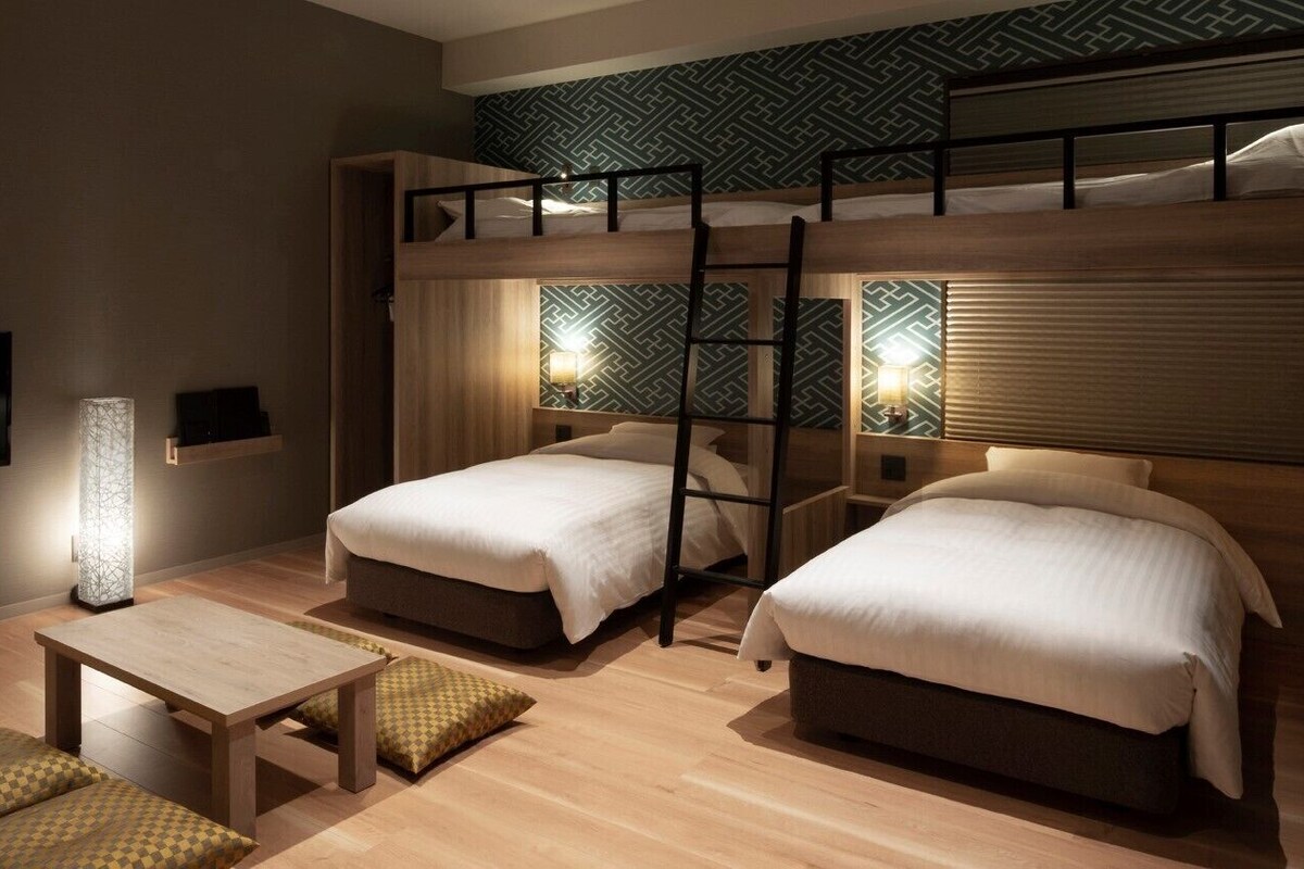 A room with two bunk beds, a bedside table, a lamp, and a patterned wall.