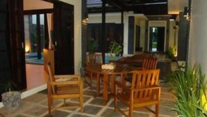 An indoor patio area with a wooden table and chairs, stone flooring, and potted plants. - Luxio Hotel Sorong (Sorong)