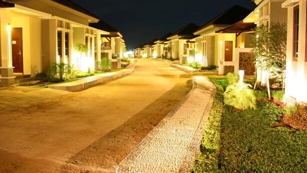 A row of modern, well-lit residential buildings at night with a paved walkway and landscaped gardens. - Luxio Hotel Sorong (Sorong)