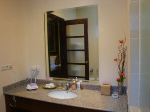 A bathroom with a granite countertop, a white sink, a hairdryer, a mirror, and a vase with flowers. - Luxio Hotel Sorong (Sorong)
