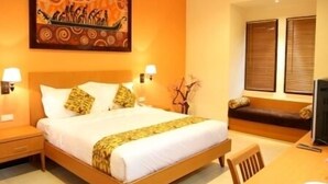 A hotel room with a large bed, two bedside lamps, a wooden headboard, a decorative painting, a sofa, and a television. - Luxio Hotel Sorong (Sorong)