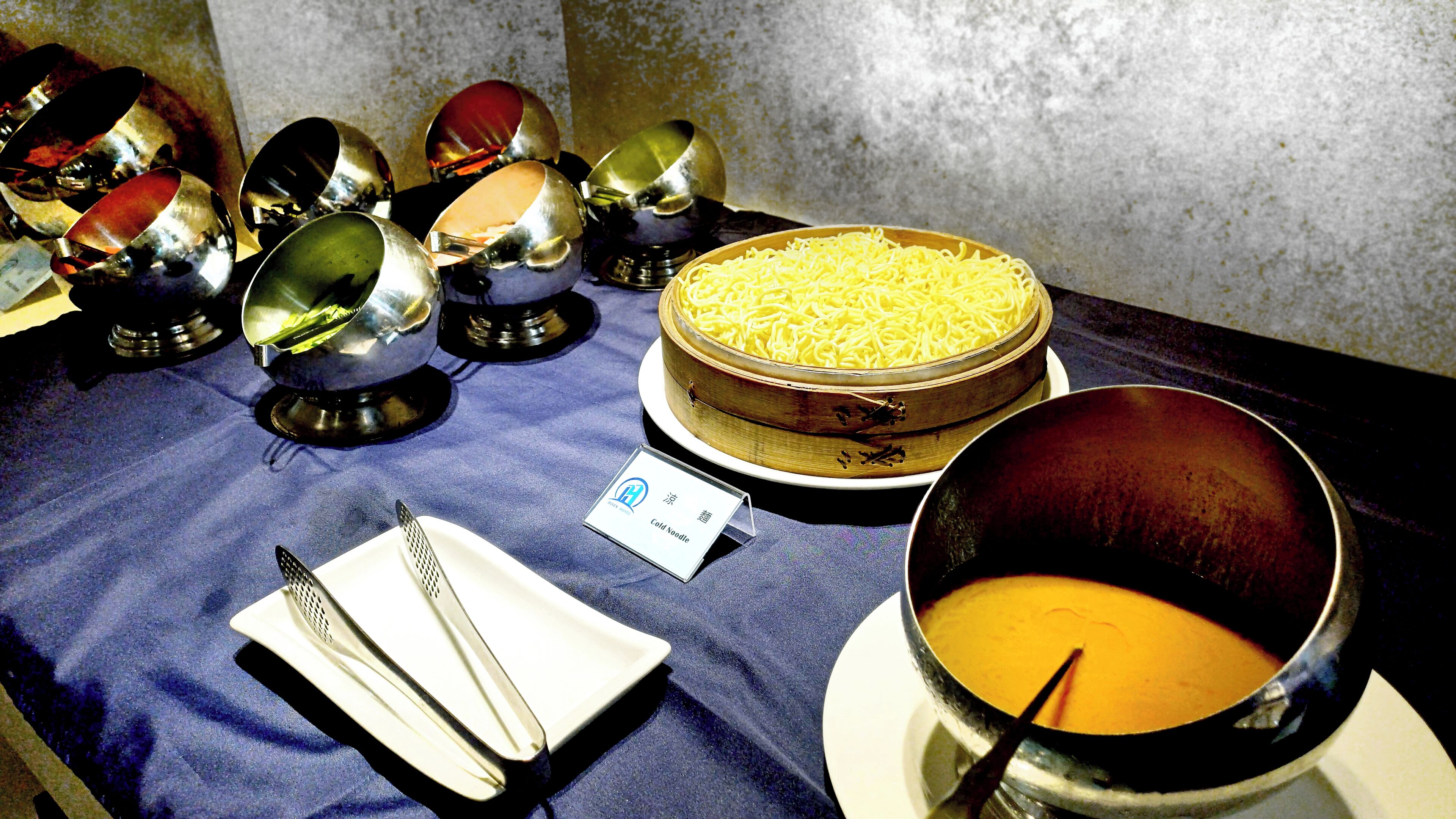 A table with a bowl of soup, a plate of noodles, and several metal bowls.