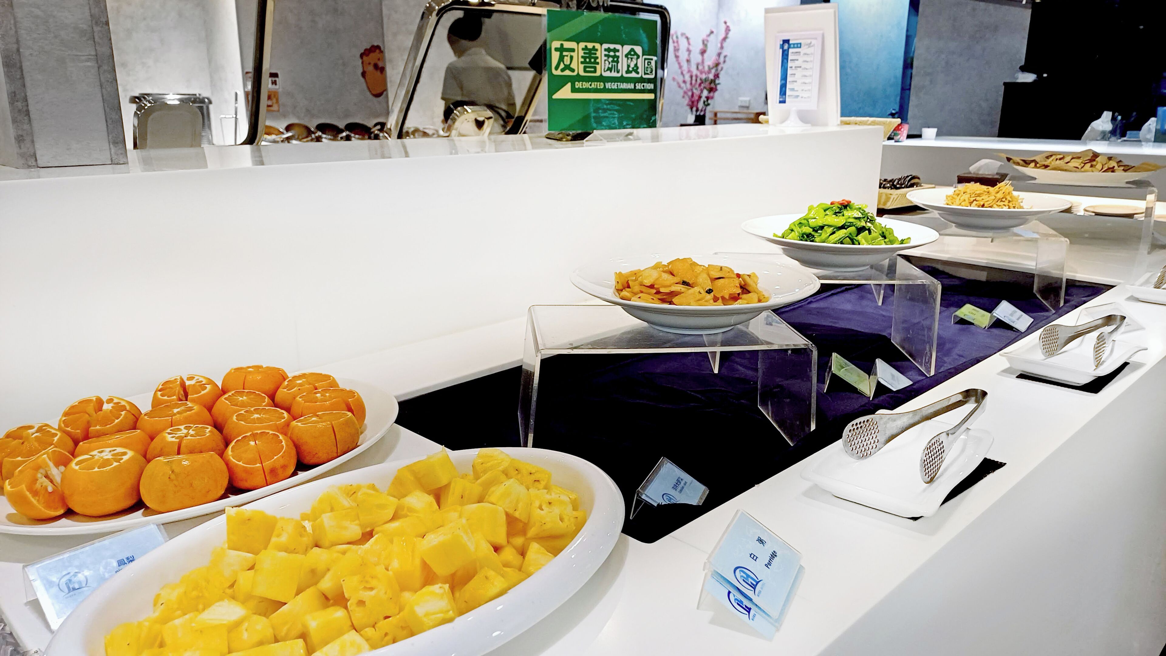 A buffet with various food items including oranges, pineapple, and other dishes, with a dedicated vegetarian section.
