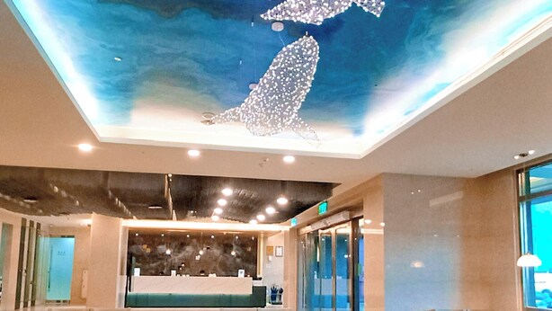 Un hall d’hôtel moderne avec une fresque au plafond, des espaces de détente et un comptoir d’accueil.