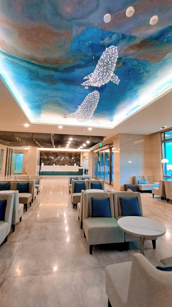 Un moderno vestíbulo de hotel con un mural en el techo, zonas de estar y una recepción.