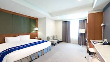 A hotel room with a large bed, a desk, a chair, and a sofa.