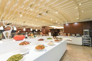 Ein Bereich mit Buffet und vielfältigen Speisen, ein modernes Decken-Design und eine Küche im Hintergrund.