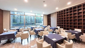 Une salle de conférence équipée de tables et de chaises, de grandes fenêtres et d’une bibliothèque.