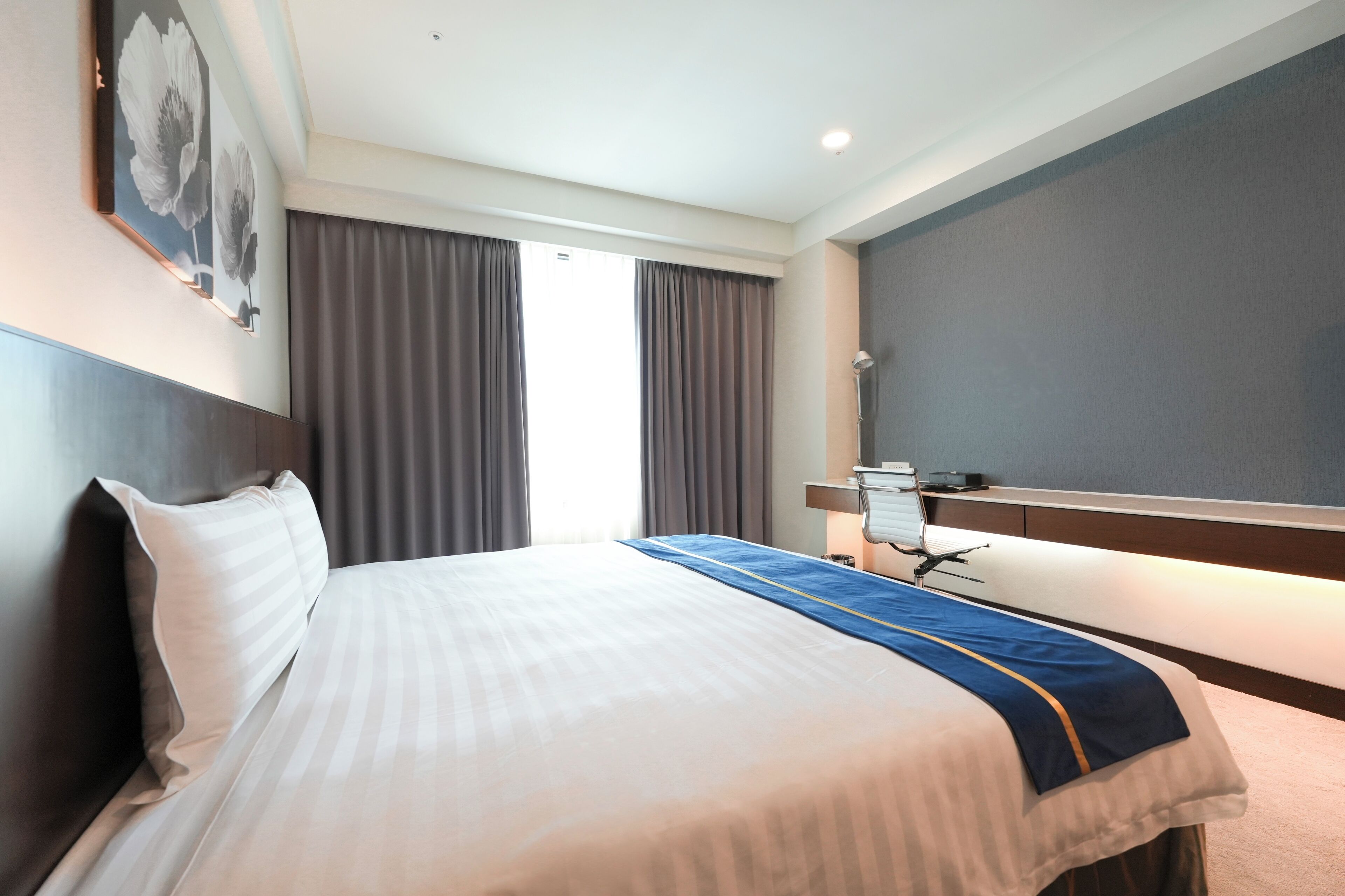 Ein Hotelzimmer mit einem großen Bett, einem Nachttisch, einem Spiegel und einem Fenster mit Vorhängen.