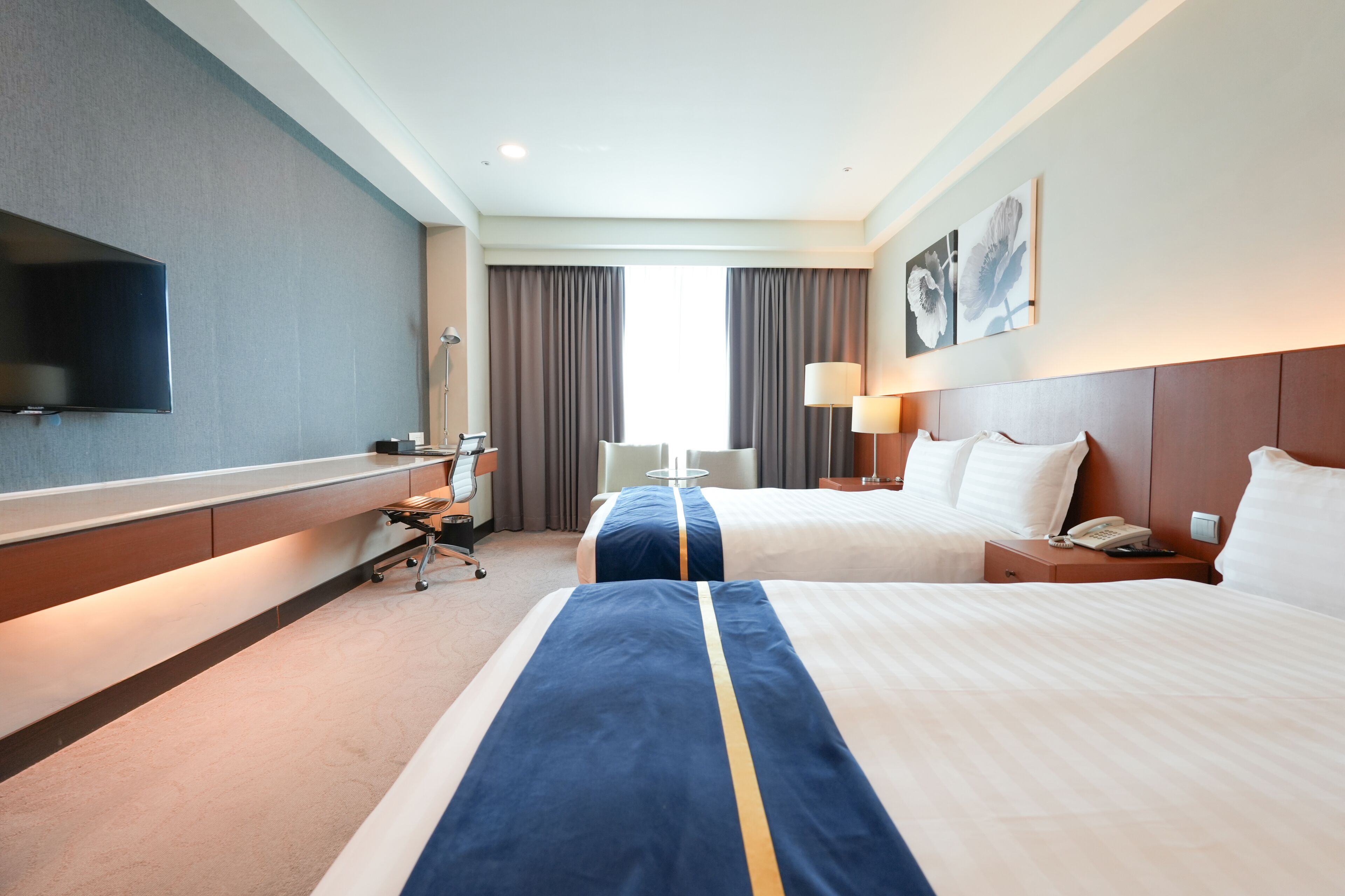 A hotel room with two beds, a flat-screen TV, a desk, and a chair.