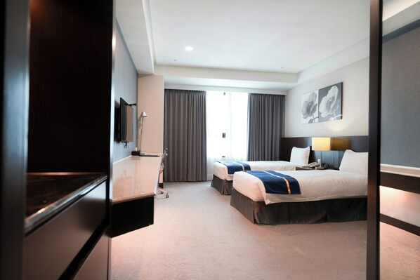 Ein Hotelzimmer mit zwei Betten, einem Fernseher, einem Schreibtisch und einem Fenster mit Vorhängen.