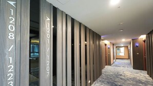 Un couloir d’hôtel avec des portes numérotées, une moquette à motifs et un éclairage lumineux au plafond.