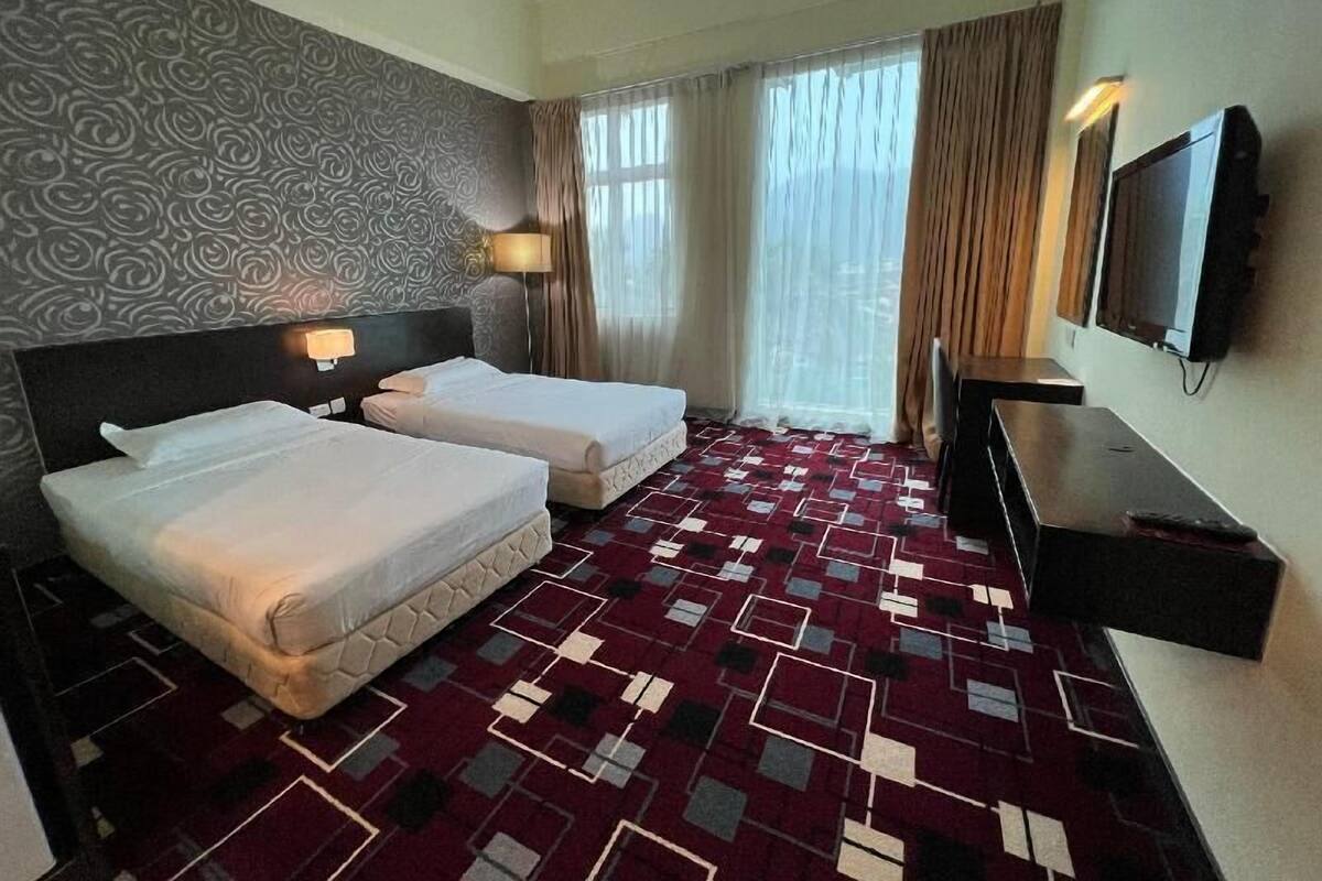 A hotel room with two beds, a TV, a desk, and a patterned carpet.