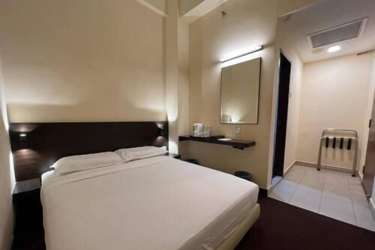 A hotel room with a bed, a nightstand, a mirror, a shelf with toiletries, and a radiator.