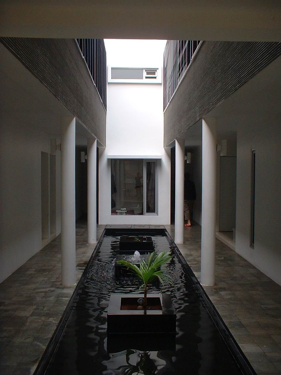 A corridor with a central water feature, white pillars, and a view of a building in the distance.